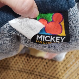 May include: A blue and grey towel with a Mickey Mouse logo. The logo is yellow, red, green and blue. The text on the logo reads "Mickey Unlimited".
