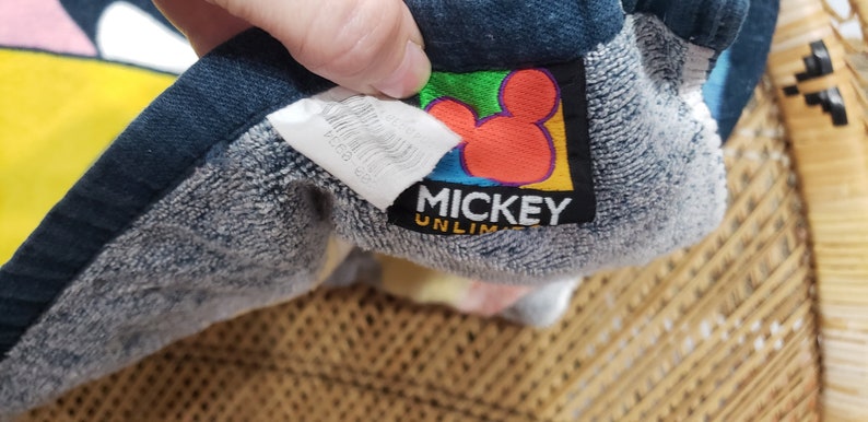 May include: A blue and grey towel with a Mickey Mouse logo. The logo is yellow, red, green and blue. The text on the logo reads "Mickey Unlimited".