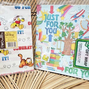 Puede incluir: Dos hojas de papel de regalo con el tema de Garfield. Una hoja presenta a Garfield y Odie con el texto "Go For It!" y "Congratulations". La otra hoja presenta un arco&iacute;ris, nubes y el texto "Just For You".