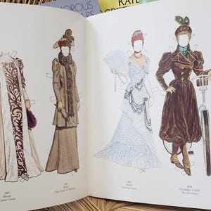 Puede incluir: Libro abierto con mu&ntilde;ecas de papel vintage. Las mu&ntilde;ecas visten trajes hist&oacute;ricos, incluyendo vestidos largos, abrigos y sombreros. Las ilustraciones son a color y presentan dise&ntilde;os detallados. Se ve un libro azul con una mujer vestida de negro.