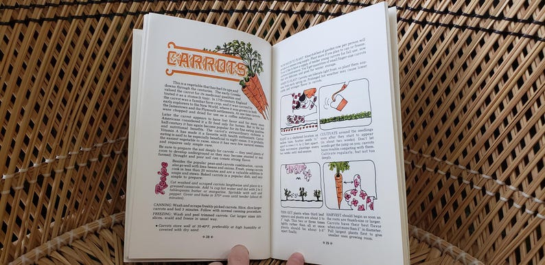 May include: Open book with text and illustrations about carrots. The left page features the title "CARROTS" in orange script with a drawing of carrots. The right page has illustrations of planting and growing carrots. The book is open on a woven surface.