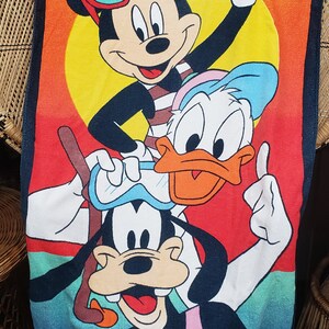 May include: A colourful beach towel featuring Mickey Mouse, Donald Duck, and Goofy wearing sunglasses and enjoying the beach. The towel has the text "St. Thomas Virgin Islands" at the top.