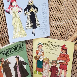 Puede incluir: Tres libros de mu&ntilde;ecas de papel vintage. Los t&iacute;tulos incluyen "Glamorous Movie Stars of the Thirties", "Great Fashion Designs of the Forties" y "Kate Greenaway Paper Dolls". Los libros presentan ilustraciones de moda y estrellas de cine.