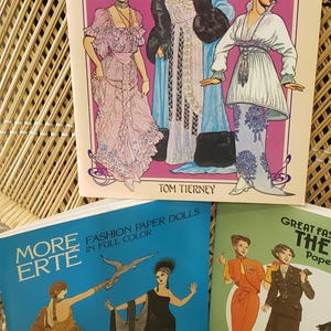 Puede incluir: Una colecci&oacute;n de libros de mu&ntilde;ecas de papel vintage con dise&ntilde;os de moda. Las portadas muestran ilustraciones de mujeres con elegantes vestidos y disfraces de diferentes &eacute;pocas. Los t&iacute;tulos incluyen "Great Fashion Designs of the Belle Epoque" y "More Erte Fashion Paper Dolls."