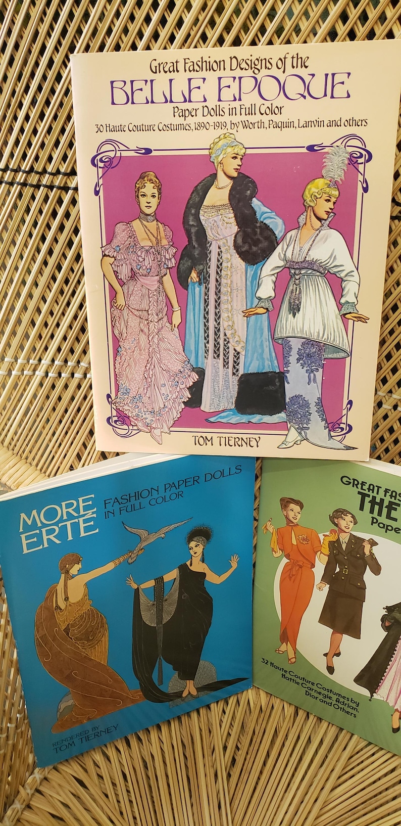 Puede incluir: Una colecci&oacute;n de libros de mu&ntilde;ecas de papel vintage con dise&ntilde;os de moda. Las portadas muestran ilustraciones de mujeres con elegantes vestidos y disfraces de diferentes &eacute;pocas. Los t&iacute;tulos incluyen "Great Fashion Designs of the Belle Epoque" y "More Erte Fashion Paper Dolls."