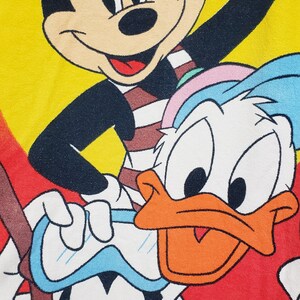 May include: A colourful illustration of Mickey Mouse, Donald Duck, and Goofy wearing sunglasses and swimming gear. Mickey is wearing red sunglasses, Donald Duck is wearing a blue and white swimming cap, and Goofy is wearing blue goggles. The background is a yellow and orange ombre.