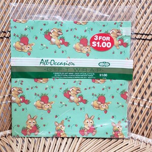 Puede incluir: Una hoja de papel de regalo verde con un patr&oacute;n de conejos y fresas. El texto "All-Occasion Gift Wrap" y "3 por $1.00" est&aacute; impreso en la hoja.