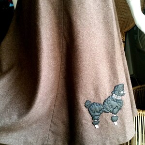 May include: A brown wool skirt with a black poodle applique. The skirt is a-line and has a high waist.