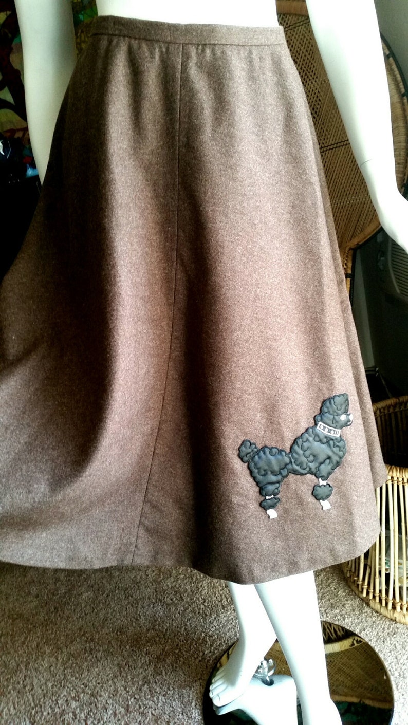 May include: A brown wool skirt with a black poodle applique. The skirt is a-line and has a high waist.
