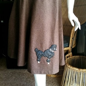 May include: A brown wool skirt with a black poodle applique. The poodle is wearing a white collar with the text "La Belle" on it.