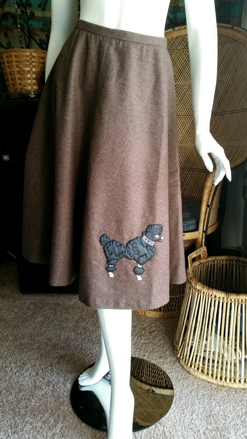 May include: A brown wool skirt with a black poodle applique. The poodle is wearing a white collar with the text "La Belle" on it.