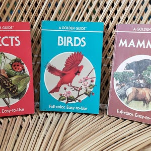 May include: Three vintage "A Golden Guide" books: "Insects" in red, "Birds" in turquoise, and "Mammals" in maroon. Each book features a colorful illustration of the subject and the text "Full-color, Easy-to-Use".