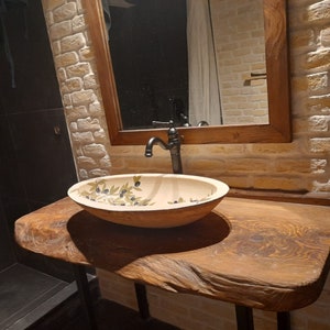 Peut inclure: Une vasque de salle de bain en bois rustique avec un lavabo en c&eacute;ramique blanche orn&eacute; d'un motif floral. Le lavabo est dot&eacute; d'un robinet noir et est install&eacute; sur un fond de briques blanches.