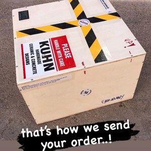 Puede incluir: Una caja de madera con cinta de advertencia negra y amarilla y una etiqueta roja que dice "PLEASE HANDLE WITH CARE". La caja est&aacute; etiquetada con "KUHN HANDMADE CERAMIC & CONCRETE DESIGNS" y "GERMANY".