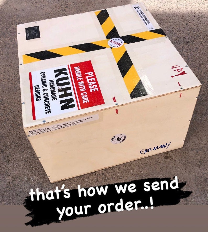 Puede incluir: Una caja de madera con cinta de advertencia negra y amarilla y una etiqueta roja que dice "PLEASE HANDLE WITH CARE". La caja est&aacute; etiquetada con "KUHN HANDMADE CERAMIC & CONCRETE DESIGNS" y "GERMANY".