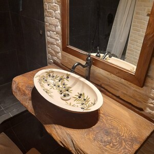 Peut inclure: Un lavabo de salle de bain en c&eacute;ramique blanche avec un motif de branche d'olivier. Le lavabo est mont&eacute; sur un comptoir en bois rustique.