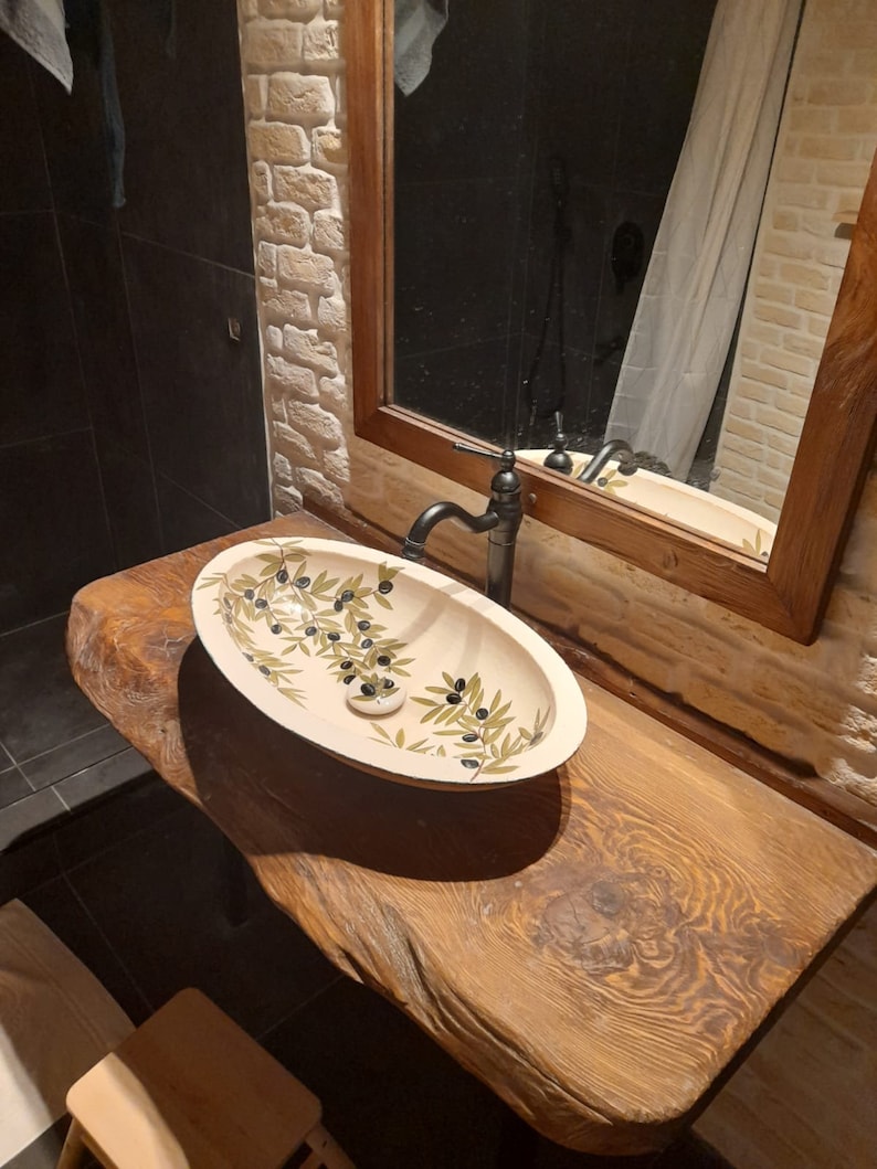 Peut inclure: Un lavabo de salle de bain en c&eacute;ramique blanche avec un motif de branche d'olivier. Le lavabo est mont&eacute; sur un comptoir en bois rustique.
