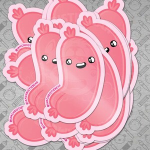 May include: A stack of pink vinyl stickers featuring a cartoon sausage with a smiling face and a pink background. The stickers have the text "@iamchristiebear" on them.