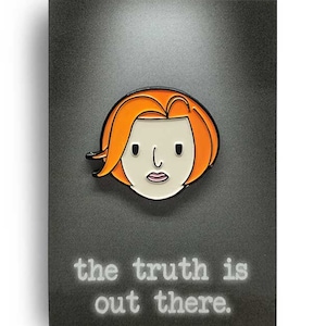 May include: A black and white enamel pin featuring a cartoon illustration of a woman with orange hair. The text "the truth is out there." is printed below the image.