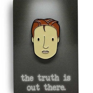 May include: A black and white enamel pin featuring a cartoon character with red hair and the text "the truth is out there."