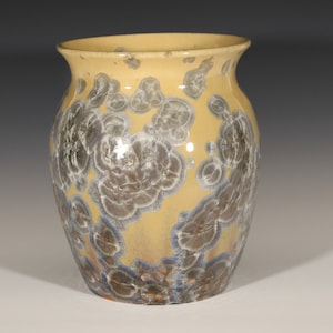 Könnte beinhalten: Eine gelbe Keramikvase mit einem einzigartigen, wirbelnden Muster aus Grau und Blau. Die Vase hat einen runden Körper und eine breite Öffnung.
