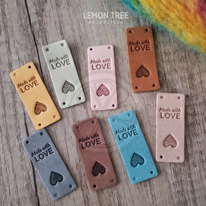 May include: Nine leather labels with the text "Made with Love" and a heart-shaped design. The labels are in various colours, including brown, beige, pink, blue, and grey.