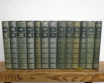 Puede incluir: Una colección de trece libros de tapa dura alineados, con lomos de color verde oscuro, patrones decorativos dorados y texto negro claro que muestra varios títulos literarios clásicos y nombres de autores.