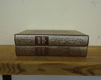 Puede incluir: Dos libros de tapa dura apilados sobre una superficie de madera. Los libros están encuadernados en cuero marrón con diseños plateados ornamentados y el título "Gone With The Wind" es visible. Los libros están en excelente estado.