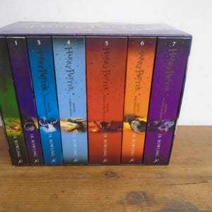 May include: A boxed set of seven Harry Potter books. The spines are various colours, including green, purple, orange, and blue. The titles and author, J.K. Rowling, are visible on the spines. The books are in a dark blue box.