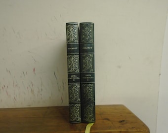 Puede incluir: Dos libros de tapa dura de color verde oscuro titulados Anna Karenina de Tolstói, volúmenes I y II. Los lomos presentan intrincados patrones decorativos de color dorado, detalles en relieve y letras claras. Los libros están colocados de pie.
