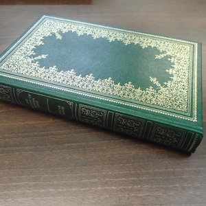 Può includere: Un libro rilegato in verde con dettagli dorati sulla copertina. Il titolo del libro è "Il ritratto di Dorian Gray" di Oscar Wilde.