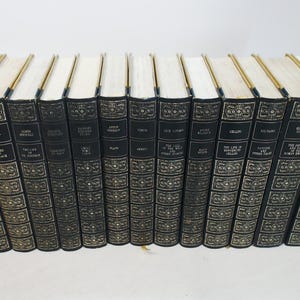 May include: A set of hardcover books with black covers and gold lettering. The spines display titles and author names. The page edges are cream-coloured, and the top edges are gilded. The books are arranged in a row.