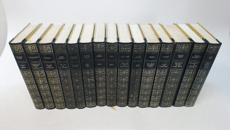 May include: A set of hardcover books with black covers and gold lettering. The spines display titles and author names. The page edges are cream-coloured, and the top edges are gilded. The books are arranged in a row.