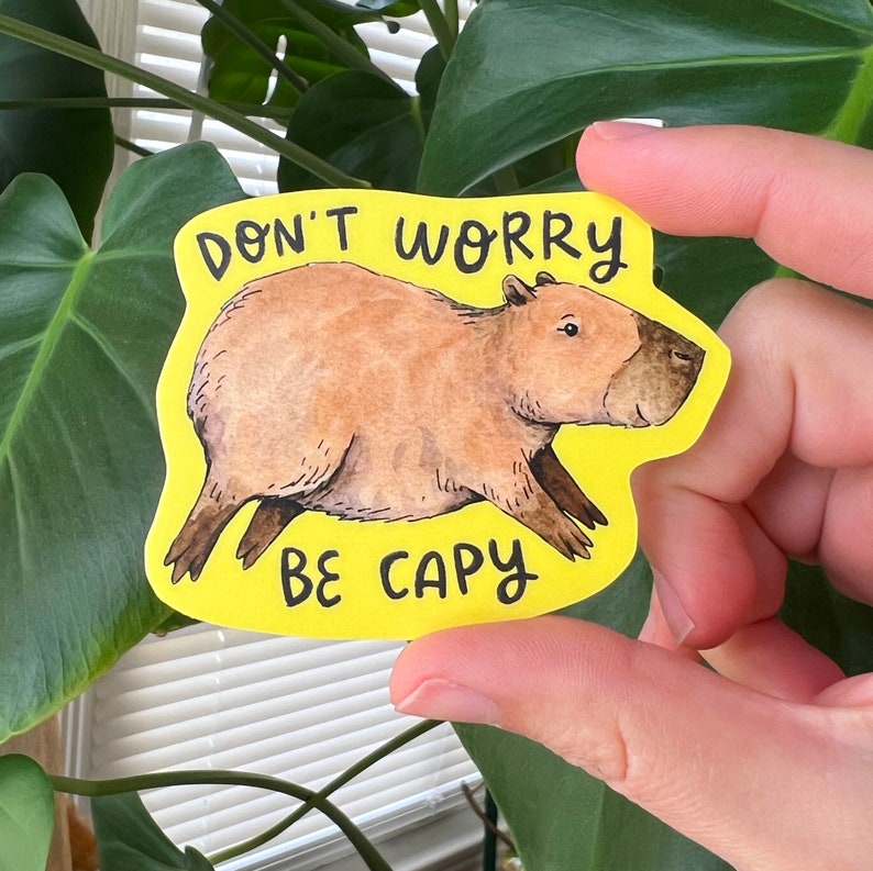 May include: A yellow sticker with a watercolor illustration of a capybara. The text "DON'T WORRY BE CAPY" is written in black. The capybara is brown with dark brown legs and a dark brown nose.