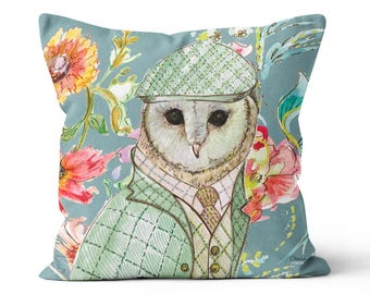 May include: Square cushion with a watercolour illustration of a barn owl in a green tweed suit and cap. The owl is set against a teal background with floral accents in pink, orange, and yellow.