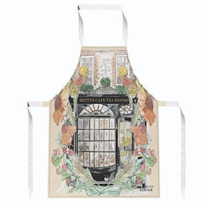 May include: A beige apron with a watercolor illustration of a cafe storefront with the text "Betty's Cafe Tea Rooms". The storefront is surrounded by floral designs in shades of orange, yellow, and green.