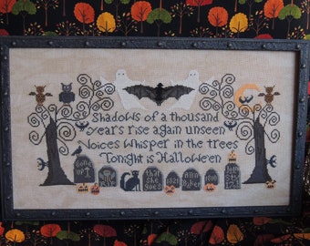 May include: A cross-stitch embroidery with a Halloween theme. The design features a black bat, two ghosts, two owls, two trees, and a crescent moon. The text reads "Shadows of a thousand years rise again unseen" and "Voices whisper in the trees Tonight is Halloween".