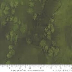 May include: A close-up of a fabric with a mottled, watercolor-like pattern in shades of green and olive. A ruler is at the bottom, showing measurements in inches. The fabric has a textured appearance.