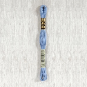 以下が含まれることがあります： DMC 刺しゅう糸 794番の色、薄い青色の糸です。糸は白い厚紙のボビンに巻かれており、金色のラベルには「DMC 25」と書いてあります。