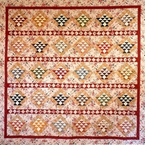 May include: A quilt with a patchwork design featuring a repeating pattern of baskets in various colours, including red, green, yellow, and blue. The background is a light beige with a speckled pattern.