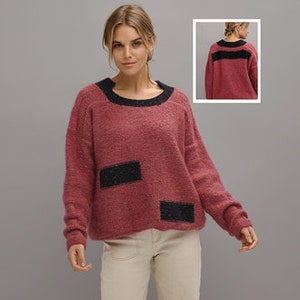 May include: A maroon sweater with black trim around the neckline and two black patches on the front. The sweater has a relaxed fit and a slightly cropped hem.