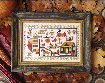 May include: A cross-stitch pattern featuring a farmhouse with a black cat on the roof, pumpkins, a scarecrow, and other autumnal details. The pattern is framed in a dark wood frame.