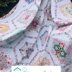 May include: A white coverlet with a floral patchwork design. The coverlet features a repeating pattern of colorful floral patches and is framed by a border of small pink flowers. The text "The Beehive Coverlet" is at the top.