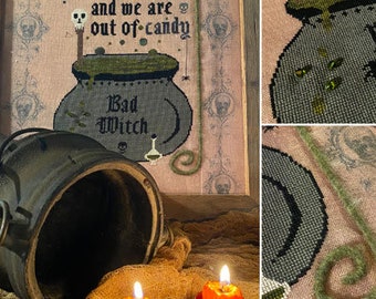May include: A cross-stitch pattern featuring a cauldron with the text "Haunted House and we are out of candy" and "Bad Witch". The pattern is on a pink background with a green and brown border.