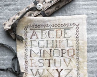 May include: A white fabric pouch with a brown embroidered alphabet and the text "Mary Anne March". The pouch is closed with a brown ribbon and has a small brown button.