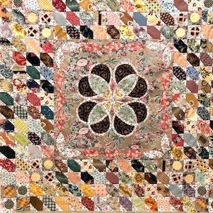 May include: A quilt featuring a large, brown and white floral design in the centre. The quilt is made up of many smaller squares of fabric in various colours and patterns.