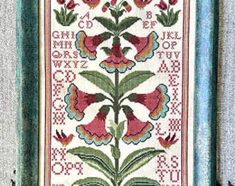May include: A cross-stitch sampler featuring a floral design with pink and white flowers and green leaves. The alphabet is embroidered in the background with the letters A through Z. The sampler is framed in a teal frame.