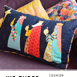 May include: A blue and black cushion with a patchwork design featuring three wise men holding gifts. The cushion has a gold trim and the text "We Three Kings" is printed below the image. The text "Cushion Pattern" and "By: Louise Papas" is printed below the image.