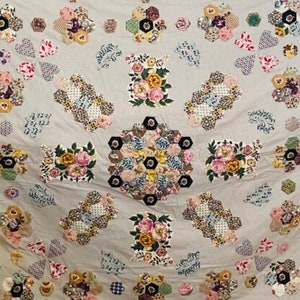 May include: A vintage quilt with a floral pattern. The quilt is made of various fabrics in shades of pink, blue, green, and white. The quilt is quilted in a traditional pattern.