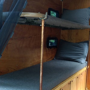 Peut inclure: Un lit superposé en bois avec un matelas et des oreillers gris. Le lit est intégré au mur d'un camping-car. Le lit supérieur est doté d'une moustiquaire en maille noire.